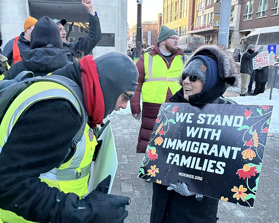 A demonstrator holding a sign that reads We Stand With Immigrant Families at a No Kings Day gathering